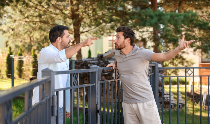 Angry neighbours having argument near fence outdoors